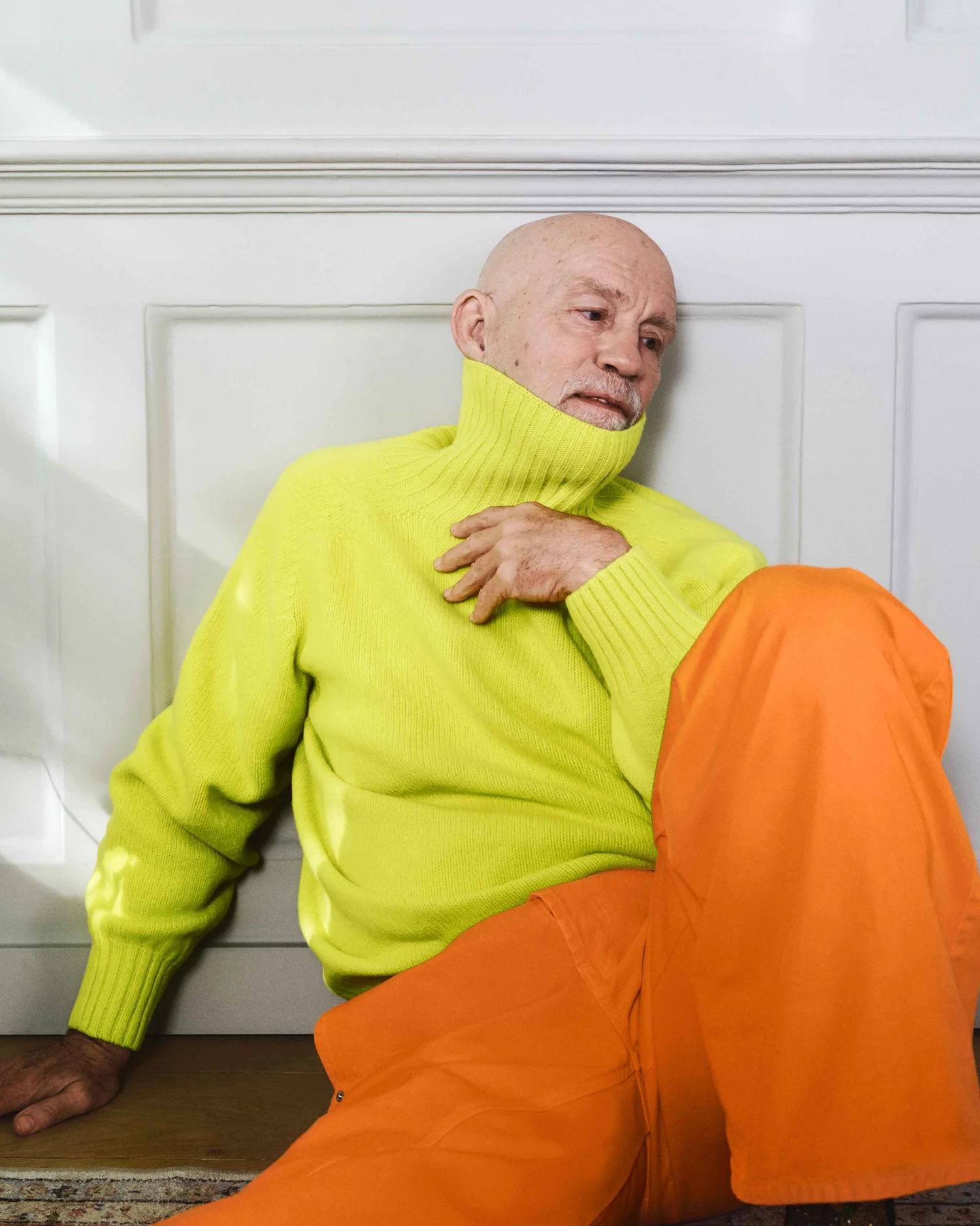 Glumac John Malkovic u naradžastim pantalonama, zelenom fluroscentnom džemperu.