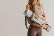 Žena drži sivu prostirku za trening.