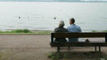 Muškarac i žena sede na klupi, ispred njih je reka.