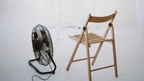 Crni ventilator pored koga stoji drvena stolica.