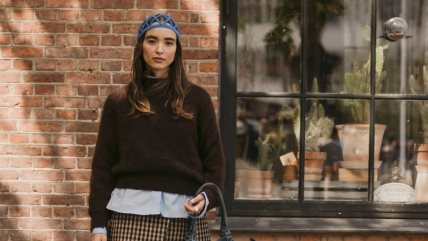 Devojka u braon funnel-neck džemperu, kratkoj pepito suknji i plavoj košulji.