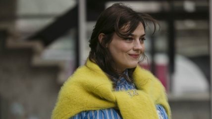 Žena nosi džemper kao aksesoar preko plave košulje.