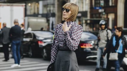 Žena u sivoj suknji i kariranoj košulji sa visokom kragnom.