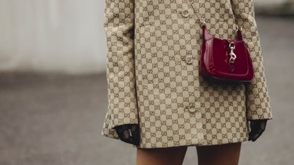 Žena u krem kratkom kaputu sa braon detaljima i bordo torbici.