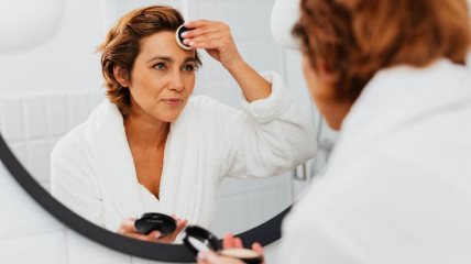 Žena ispred ogledala nanosi šminku.