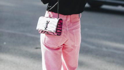 Žena u roze somotskim pantalonama, crnoj majici i YSL torbici.
