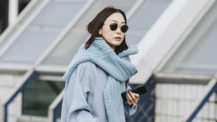 Žena u pletonom plavom kompletu i preko ramena ima prebačen džemper u sličnoj nijansi.