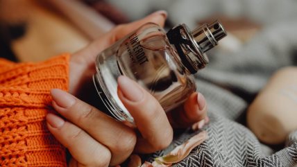 Žena u narandžastom džemperu drži bočicu parfema.