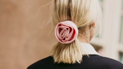 Žena u crnom džemperu i beloj košulji, sa srednjom dužinom kose vezanoj u rep sa gumicom na kojoj je roze ruža.