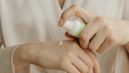 Krupan kadar na ruke. Žena nanosi kremu iz zelene tube.