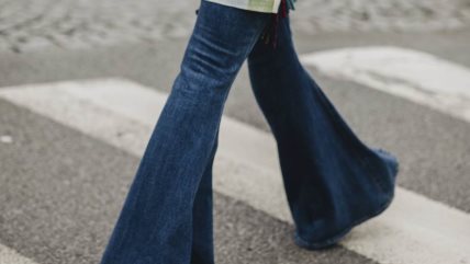 Žena u zvoncarama od tamnog teksasa prelazi preko pešačkog prelaza.