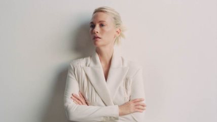 Žena u belom odelu gleda u stranu.