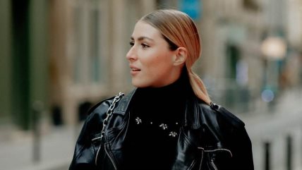 Žena koja gleda u stranu, obučena u crnu džemper rolku i kožnu jaknu iste nijanse.