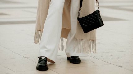Žena u beloj/bež kombinaciji, crnim cipelama i sa torbom u istoj nijansi.