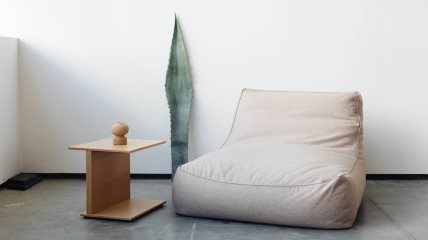 Krem mekana fotelja, veliki list kaktusa i drveni stočić u uglu sobe sa belim zidovima.