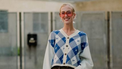 Žena u belom džemperu sa plavim romboidima i velikim ružičastim naočarima za sunce.