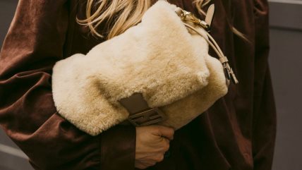 Žena u braon kombinaciji sa krem krznenom torbom.