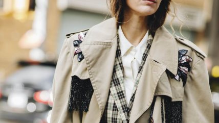 Žena u beloj košulji, kariranom sakou i krem trench mantilu.