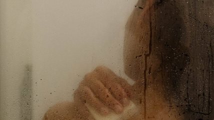 Iza zamegnjene providne kabine vidi se krupan kadar žene koja drži sapun i pere kosu.