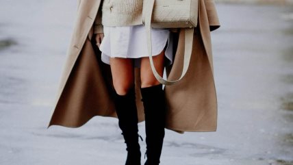 Žena u beloj mini suknji i dubokim crnim čizmama.