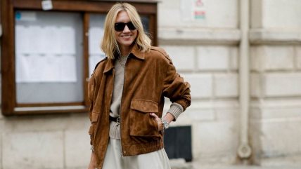 Žena u krem džemperu, beloj suknji i braon jakni od antilopa.