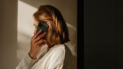 Žene stoji iz profila i drži crni mobilni telefon.