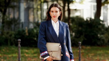 Žena u beloj košulji i teget haljina-sakou sa okruglim zlatnim dugmićima.