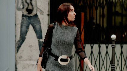 Žena u sivoj pletenoj haljini preko koje ima zakačen crni kaiš sa velikom sivom šnalom.