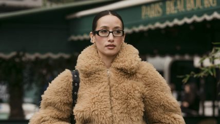 Žena sa naočarima u krem kreznenom kaputu.