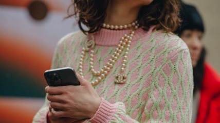 Žena u roze džemperu sa zelenim linijama i sa bisernom ogrlicom.