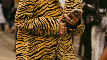 Žena u beloj majici i žutom kaputu sa animal printom.