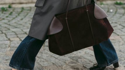 Žena u farmerkama i crnim cipelama, sa braon torbom od antilopa.