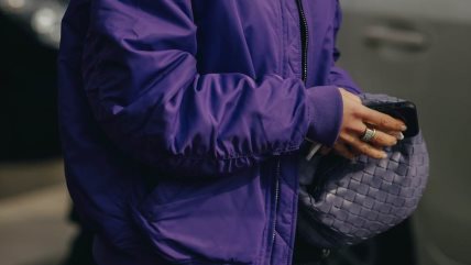 Žena u ljubičastoj jakni i sa torbicom u istoj nijansi.