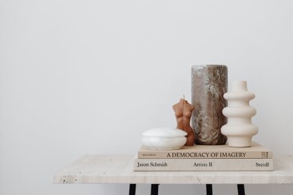 Na stolu su naslagane knjige, sveća u obliku ženskog tela i vaza.