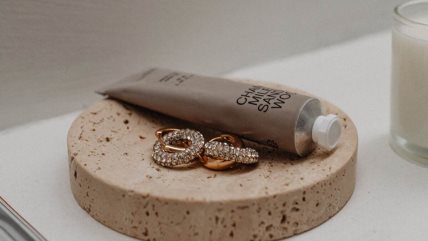 Krema za ruke na stolu porek koje stoje zlatne minđuše.