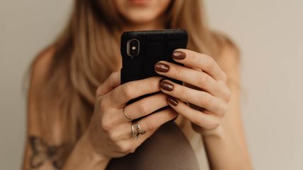 Žena sa manikirom u nijanci mocha drži telefon.