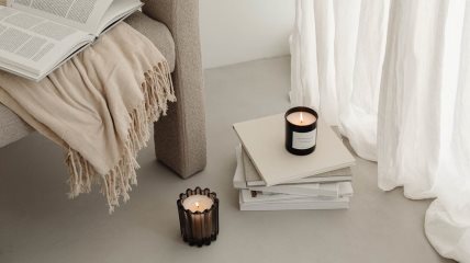 Fotelja na kojoj stoji ćebe i otvorena knjiga. Ispod nje su naslagane knjige i naređane sveće.