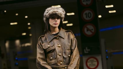 Devojka u braon kožnoj jakni sa kapom od veštačkog krzna.