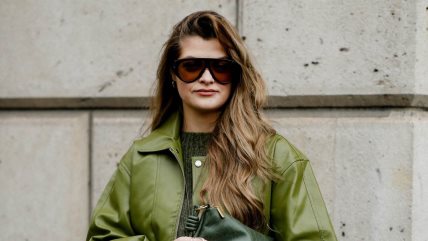 Žena u zelenoj jakni i džemperu iste boje, sa tamnim naočarima za sunce.