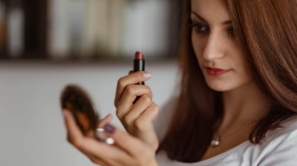 žena se šminka i drži ruž u ruci