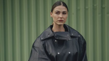 Devojka u crnom kožnom mantilu, iza nje je zelena pozadina.