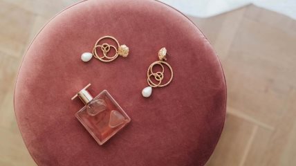 Bočica parfema i minđuše na tabureu.