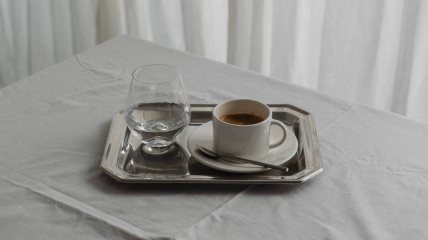 Keramička šoljica sa kafom stoji na poslužavniku od nerđajućeg čelika.