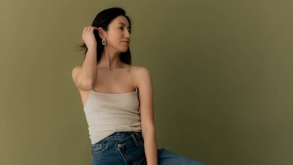 Žena stoji ispred zelene pozadine i gleda u stranu.