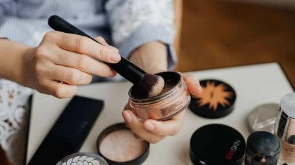 Krupan kadar na ruke žene koja drži puder u prahu i četkicu za šminkanje.