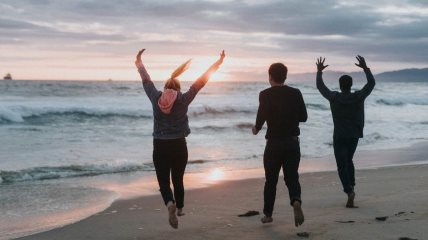 Troje ljudi srećno skače na plaži.