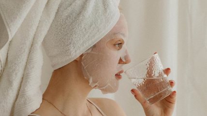 Žena sa maskom na licu pije vodu iz čaše.