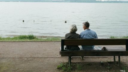 Muškarac i žena sede na klupi, ispred njih je reka.