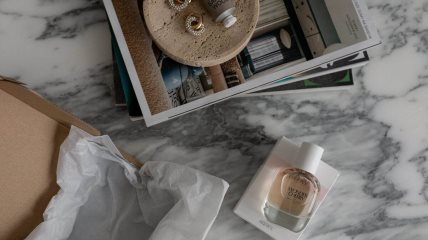 Na stolu stoje magazini, parfem i losion za telo.