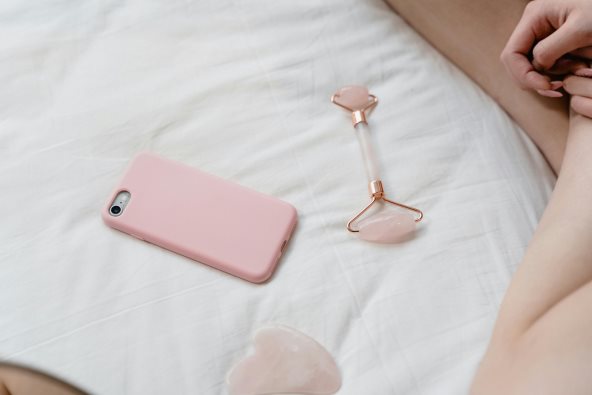 Roze telefon i skincare roler za lice na krevetu.